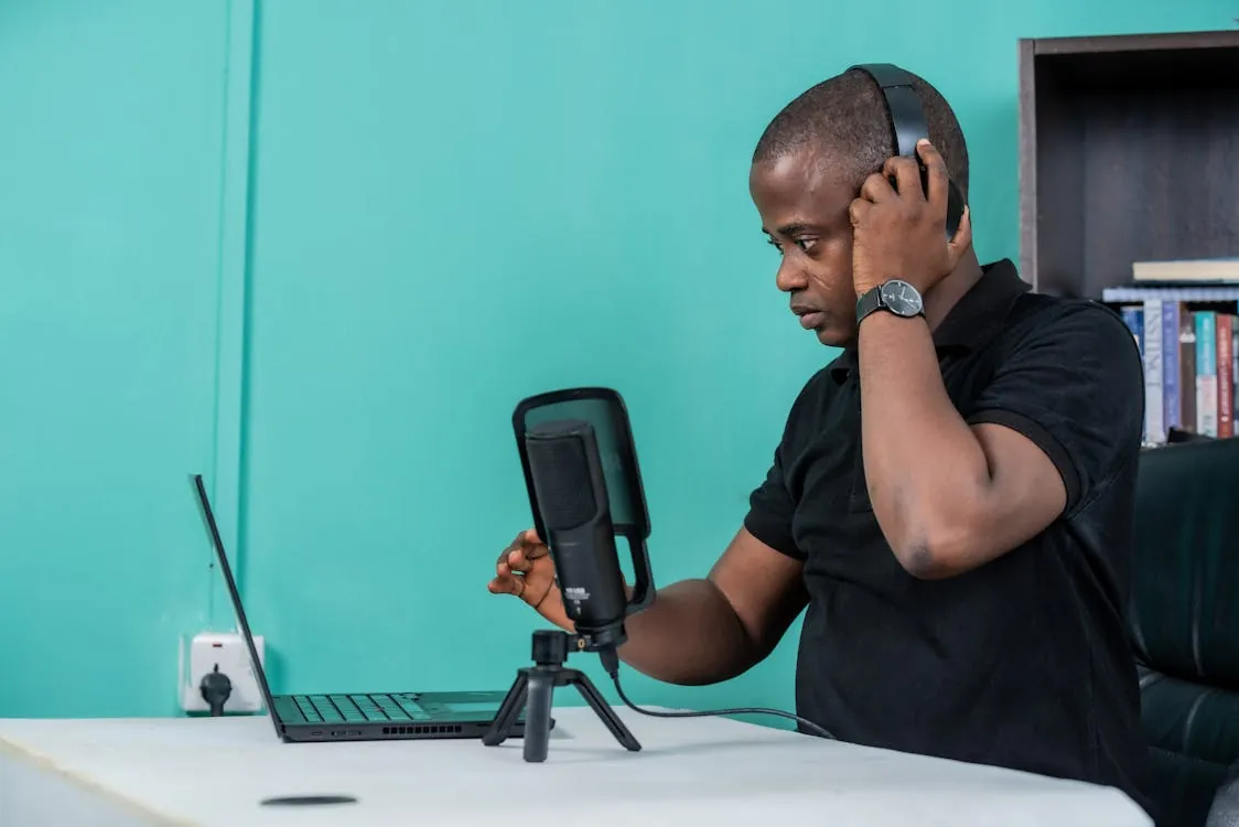 A content creator wearing headphones records a podcast at a desk with a laptop and professional microphone